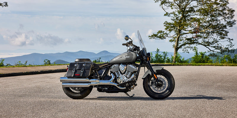 Load image into Gallery viewer, A 2026 Indian Super Chief Dark Horse motorcycle with black saddlebags and chrome exhausts parked on an asphalt road with mountains and trees in the background.