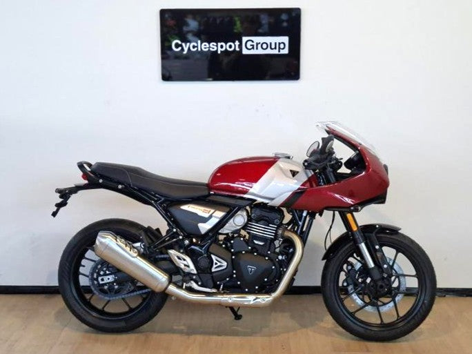 Load image into Gallery viewer, A side view of a 2026 Triumph Thruxton 400 in Carnival Red on a wooden floor, backed by a white wall with a Cyclespot Group sign in white on black.