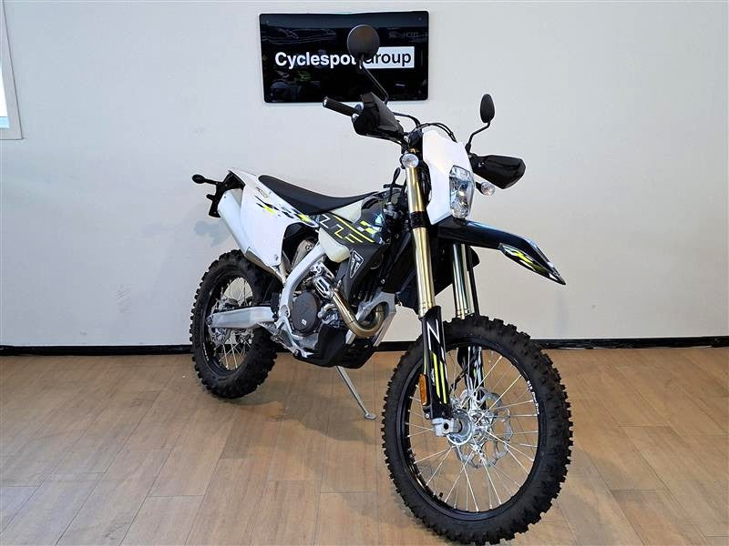 Load image into Gallery viewer, A Triumph TF 450-E dirt bike with a white, black, and yellow color scheme, displayed on a wooden floor in front of a white wall with a 'Cyclesport group' sign.
