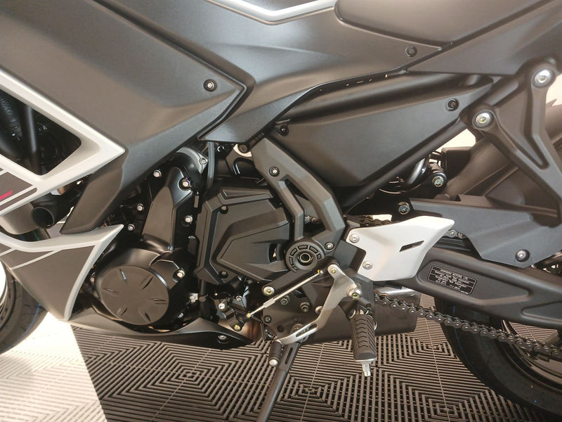 Load image into Gallery viewer, Close-up of the engine and chain of a 2026 Kawasaki Ninja ER 650 F in Pearl White, sitting atop a textured floor surface