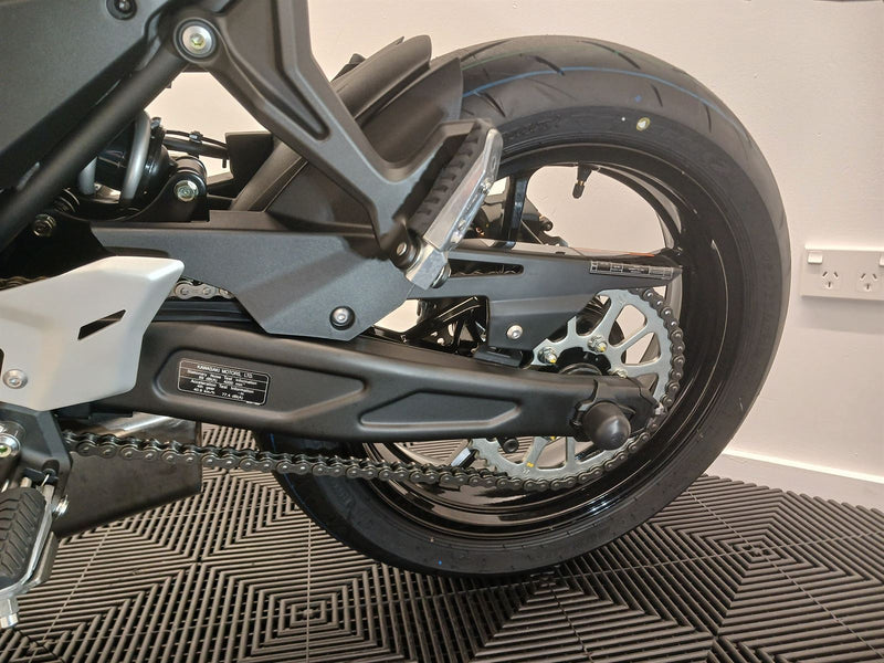 Load image into Gallery viewer, Close-up of a 2026 Kawasaki Ninja ER 650 F motorcycle's rear wheel and chain on a textured floor.