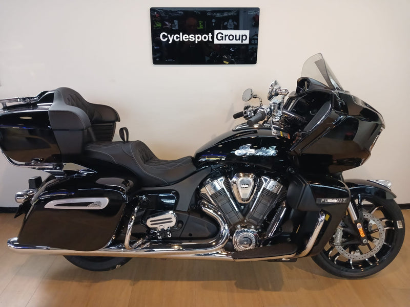 Load image into Gallery viewer, A black Indian Indian Pursuit Limited with 112 Package Motorcycle touring bike with chrome accents, displayed indoors on a wooden floor against a beige wall with a 'Cyclespot Group' sign above.