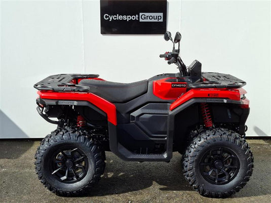 A red and black 2026 CFMOTO CFORCE C5 EPS quad bike with knobby tires, rear cargo racks, and side mirrors, parked in front of a white wall with a 'Cyclespot Group' sign.