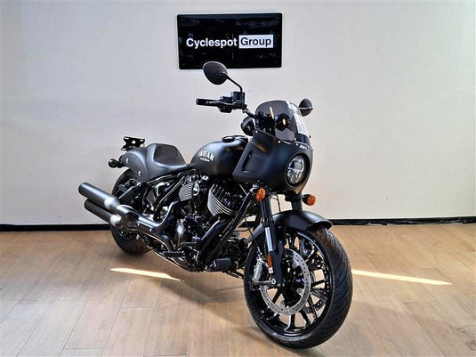 A black Indian Sport Chief motorcycle is parked indoors on a light wood floor against a white wall, with a 'Cyclespot Group' sign visible above it.