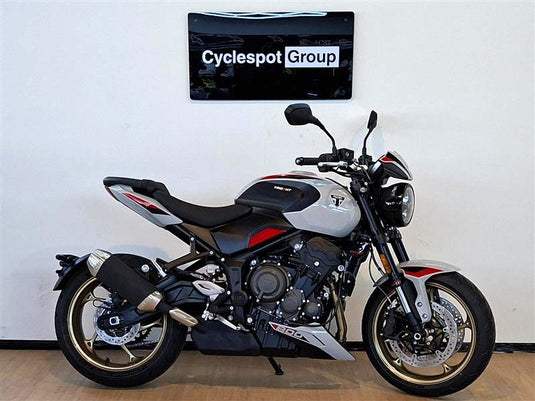 A silver and black Triumph Trident 800 motorcycle with red accents, parked indoors against a white wall with a 'Cyclespot Group' sign above it.
