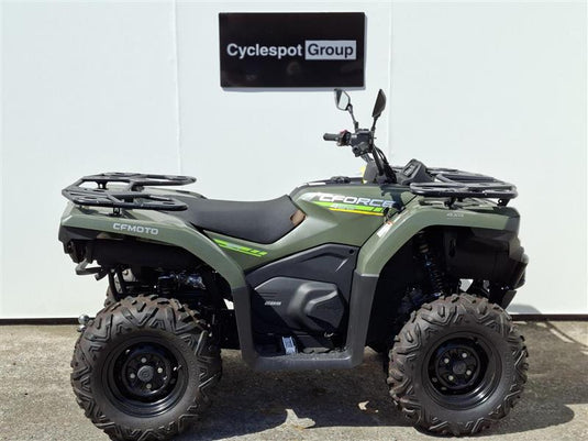 A 2025 CFMoto CFORCE 400, in Hunter Green, all-terrain vehicle (ATV) parked in front of a white wall with a 'Cyclespot Group' sign above it.