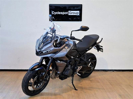 A grey  2023 Triumph Tiger Sport 660 motorcycle is parked indoors on a wooden floor against a white wall, with a 'Cyclespot Group' sign visible on the wall behind it.